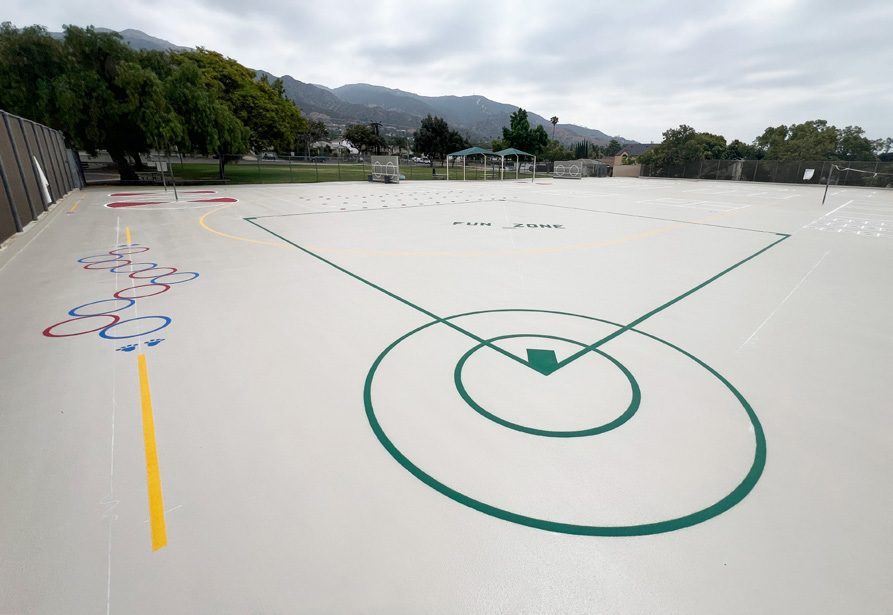School play court finished with a light DriveDeck coating and bright painted game lines, with mountains in the background